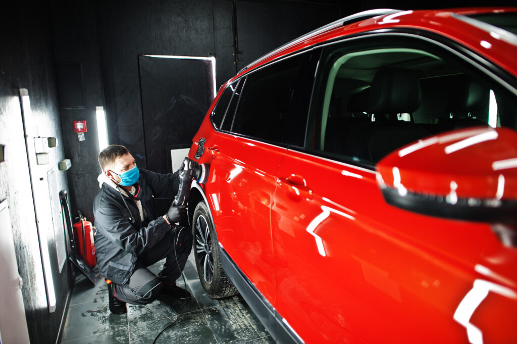 Car detailing concept. Man in face mask with orbital polisher in