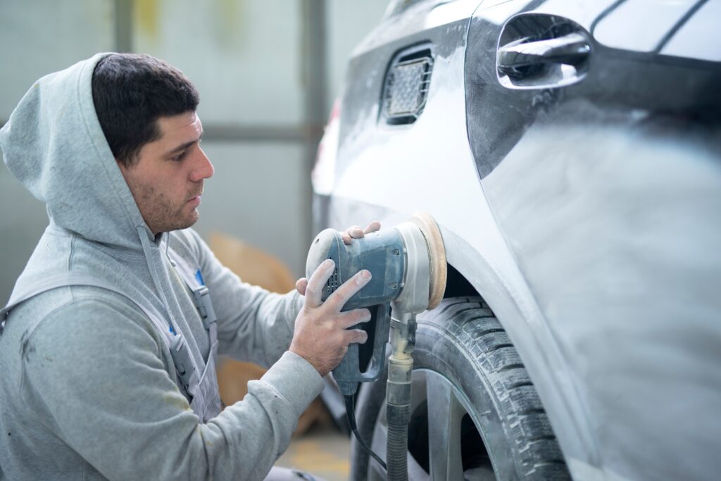 auto repairman grinding car body with machine preparing vehicle painting